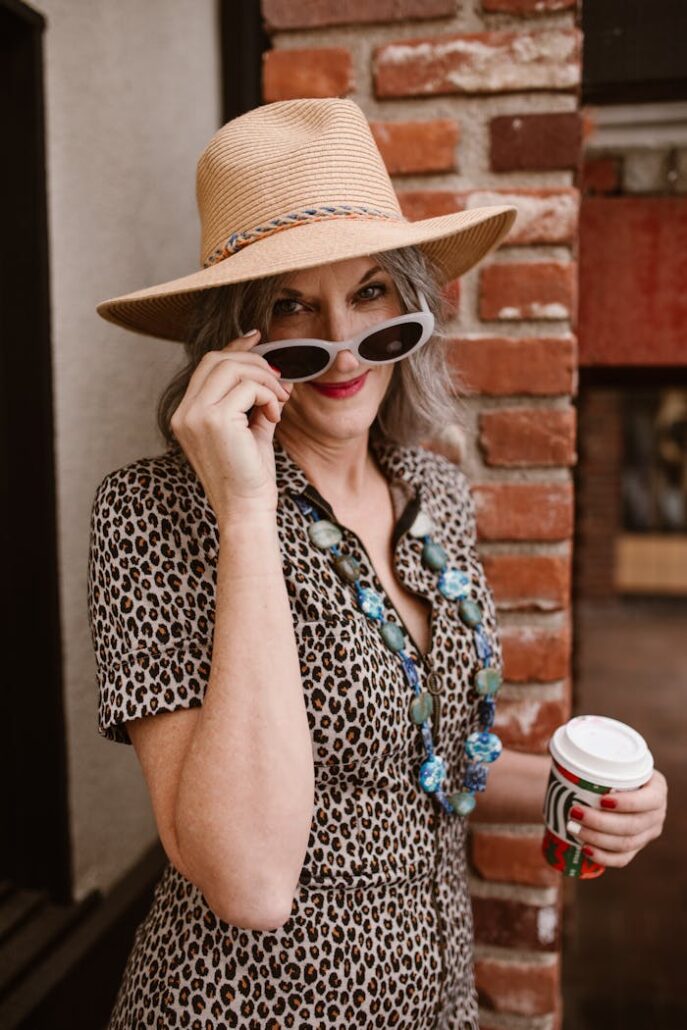 Elegant woman in leopard dress with hat and sunglasses enjoying a sunny day.